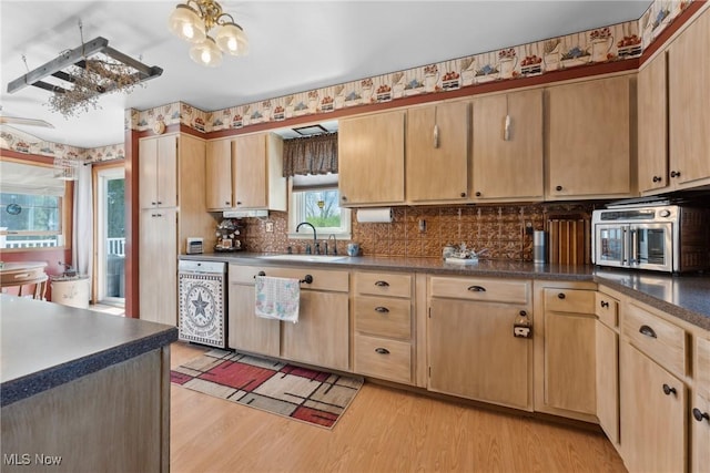 kitchen featuring light brown cabinetry, dark countertops, light wood-style floors, dishwashing machine, and a sink
