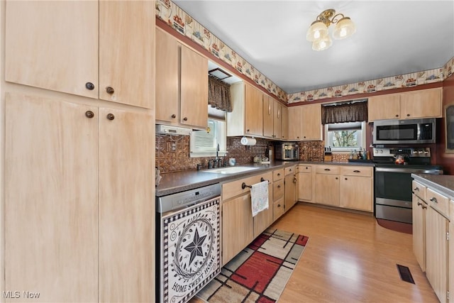 kitchen featuring light brown cabinets, dark countertops, a sink, light wood-style flooring, and stainless steel appliances