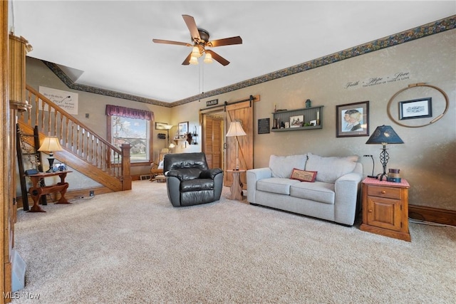 carpeted living area featuring a barn door, stairs, a ceiling fan, baseboards, and ornamental molding
