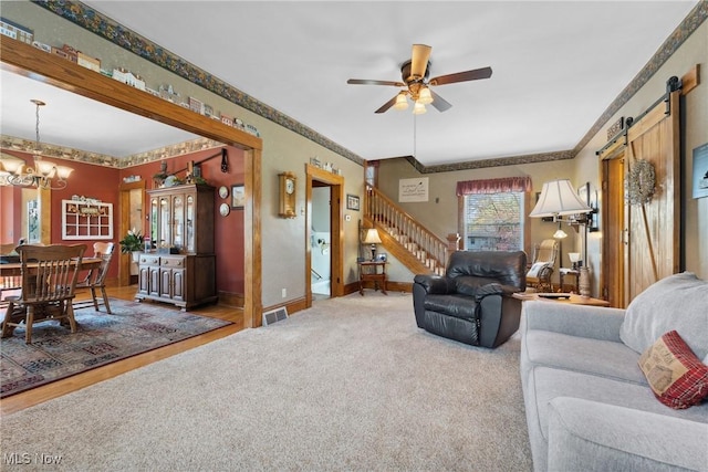 living area with a barn door, ceiling fan with notable chandelier, baseboards, visible vents, and stairway