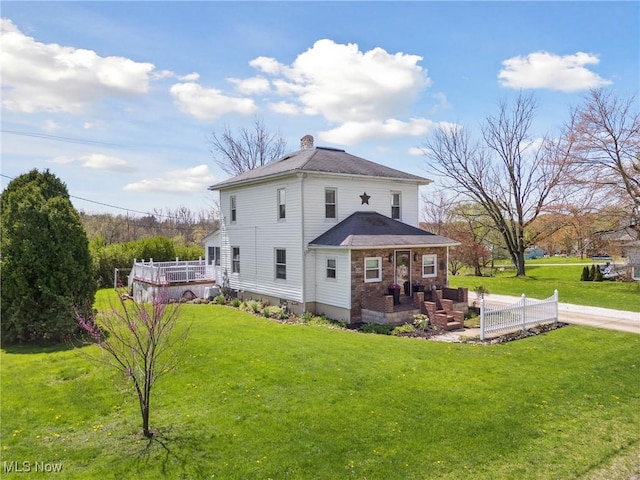 back of property with a lawn, a chimney, a shingled roof, and a deck