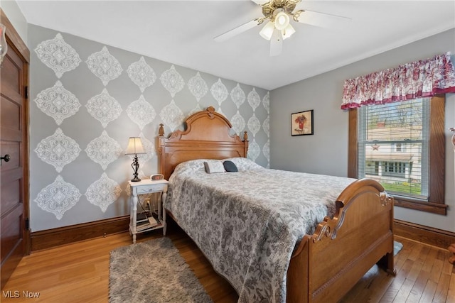 bedroom with wood-type flooring, an accent wall, baseboards, ceiling fan, and wallpapered walls