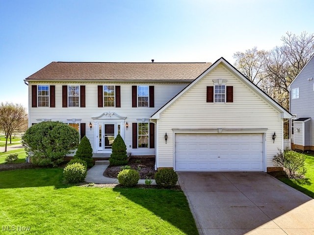 colonial inspired home featuring roof with shingles, an attached garage, driveway, and a front yard