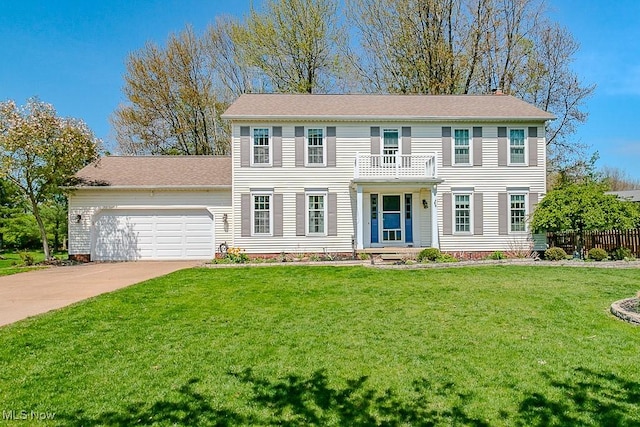 colonial house with fence, an attached garage, a front yard, concrete driveway, and a balcony