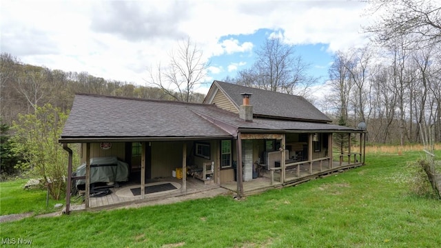 rear view of property featuring roof with shingles and a yard
