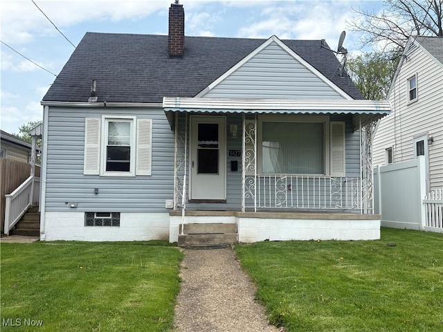 bungalow with covered porch, a chimney, roof with shingles, a front yard, and fence