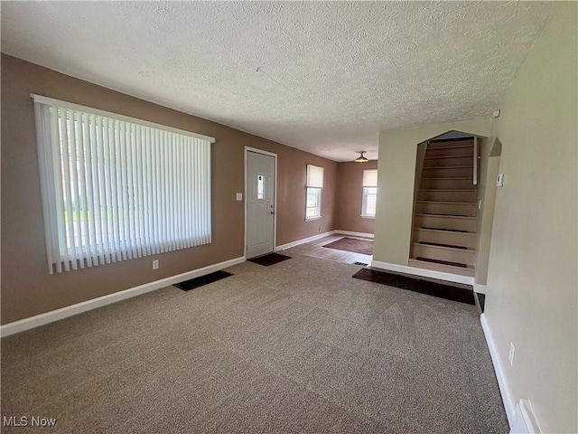 carpeted foyer entrance with baseboards, a textured ceiling, visible vents, and stairway