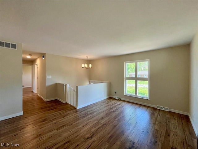 unfurnished room with dark wood-style flooring, baseboards, visible vents, and a chandelier
