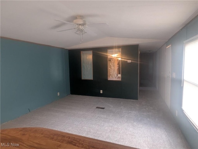 carpeted empty room with a ceiling fan, visible vents, and lofted ceiling