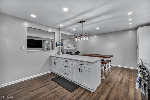 kitchen featuring dark wood-style flooring, a fireplace, baseboards, a peninsula, and white cabinetry