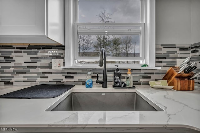 details with light stone counters, a sink, white cabinetry, and backsplash