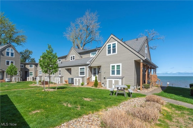 back of property with a lawn, central air condition unit, and a water view