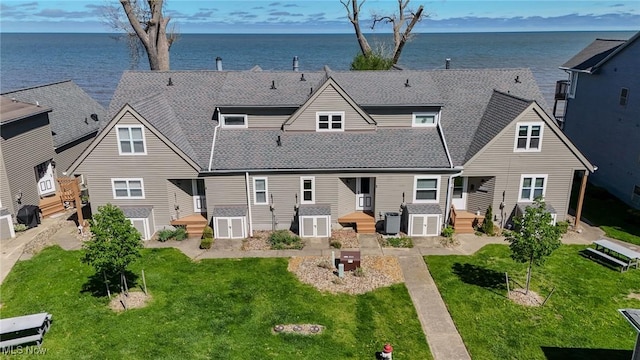 rear view of house with a lawn, a water view, and roof with shingles