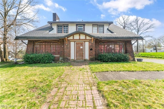 tudor-style house with brick siding, a front lawn, and a chimney