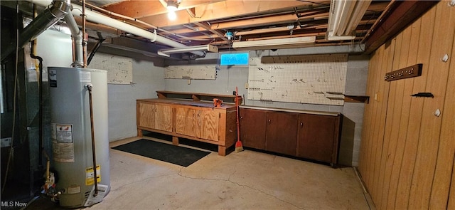 unfinished below grade area featuring concrete block wall, gas water heater, and a workshop area