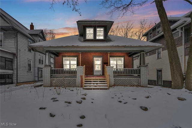 snow covered house with a porch and brick siding
