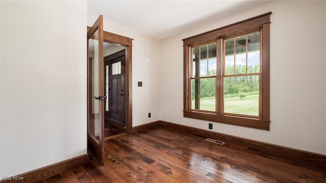 empty room featuring baseboards, dark wood-style flooring, and visible vents
