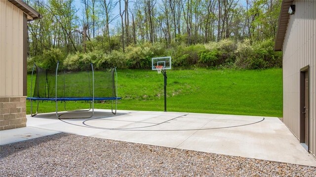 view of sport court featuring a trampoline, a yard, and basketball court