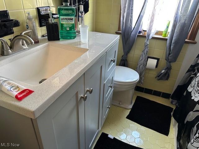 bathroom featuring toilet, tile patterned floors, tile walls, and vanity