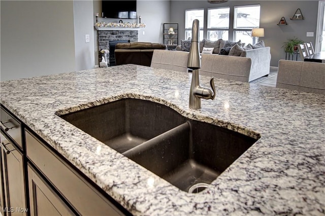 kitchen with light stone countertops, open floor plan, a sink, and a fireplace