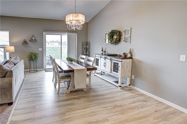 dining space with baseboards, vaulted ceiling, light wood-type flooring, and a notable chandelier