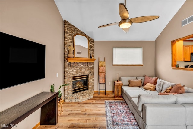 living room with ceiling fan, visible vents, a fireplace, lofted ceiling, and light wood-style floors
