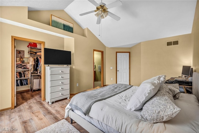 bedroom featuring a walk in closet, light wood finished floors, lofted ceiling, visible vents, and a closet