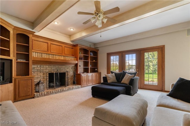 living area featuring ceiling fan, beamed ceiling, a brick fireplace, and light colored carpet