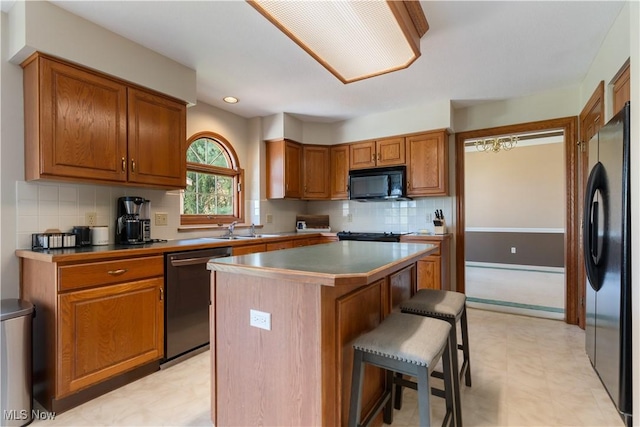kitchen featuring a breakfast bar, a sink, light floors, a kitchen island, and black appliances