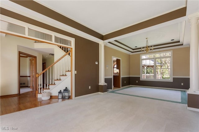 carpeted empty room with crown molding, ornate columns, baseboards, and a chandelier