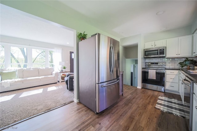 kitchen with dark wood-style flooring, appliances with stainless steel finishes, backsplash, and dark countertops