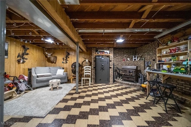 unfinished below grade area featuring a wood stove, tile patterned floors, wooden walls, and brick wall
