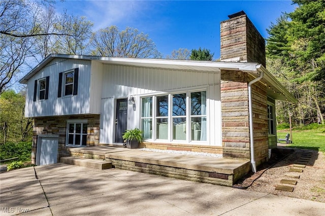 back of house featuring a garage, a chimney, driveway, and stone siding