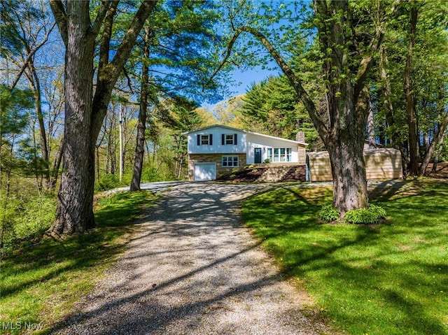 view of front of house featuring an attached garage, a chimney, a front yard, and gravel driveway