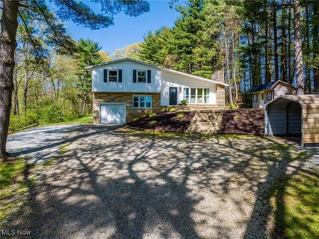 tri-level home featuring a chimney, a carport, aphalt driveway, an attached garage, and stone siding
