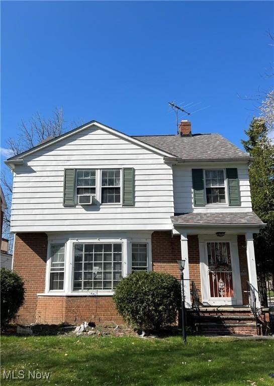 traditional-style house with a shingled roof, a chimney, a front yard, and brick siding