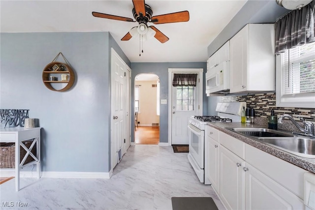 kitchen with white appliances, baseboards, ceiling fan, arched walkways, and a sink