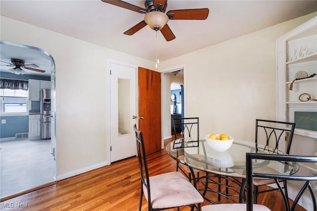 dining space featuring a ceiling fan, visible vents, arched walkways, baseboards, and light wood-style floors