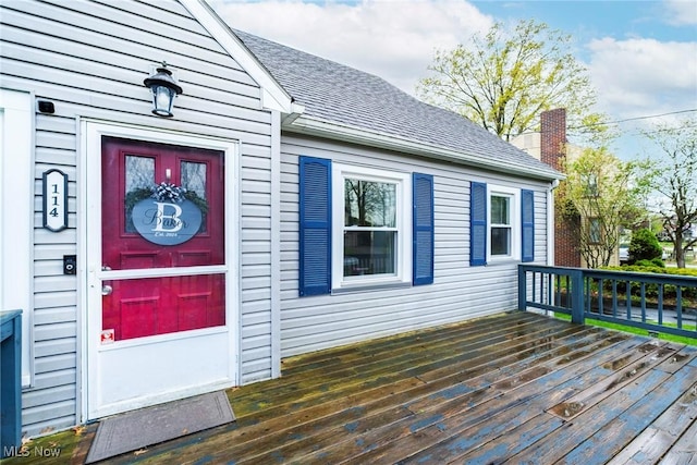 doorway to property featuring a wooden deck, a shingled roof, and a chimney