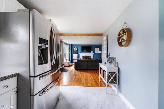 kitchen with white cabinets, dark countertops, stainless steel fridge, light wood-style floors, and open floor plan