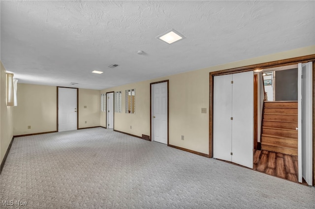 unfurnished room with stairs, a textured ceiling, baseboards, and light colored carpet