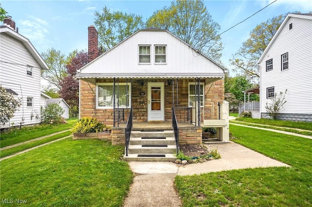 bungalow featuring covered porch, board and batten siding, a chimney, a front lawn, and stone siding