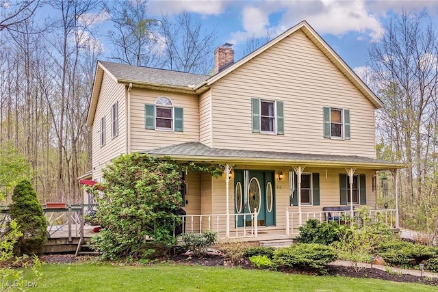 view of front of home with a porch, a front yard, and a chimney