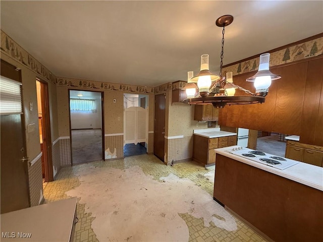 kitchen featuring brown cabinetry, white electric stovetop, wallpapered walls, light countertops, and decorative light fixtures