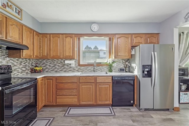 kitchen with light countertops, under cabinet range hood, tasteful backsplash, a sink, and black appliances