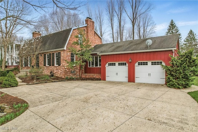 view of side of home with driveway, a chimney, a shingled roof, and a garage