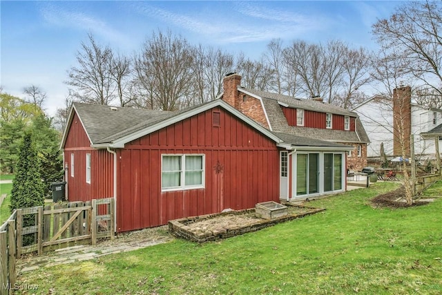 rear view of house with roof with shingles, board and batten siding, a gate, a chimney, and a lawn