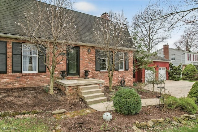 view of front of property with a garage, a chimney, brick siding, a shingled roof, and driveway