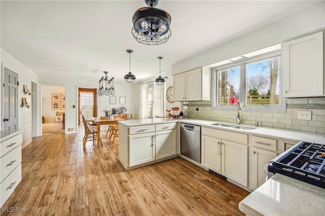 kitchen with stainless steel dishwasher, a sink, light wood-style floors, and a peninsula