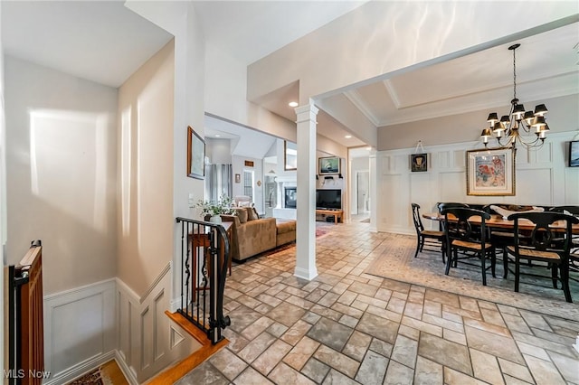 dining room featuring stone finish flooring, wainscoting, a notable chandelier, ornamental molding, and a decorative wall
